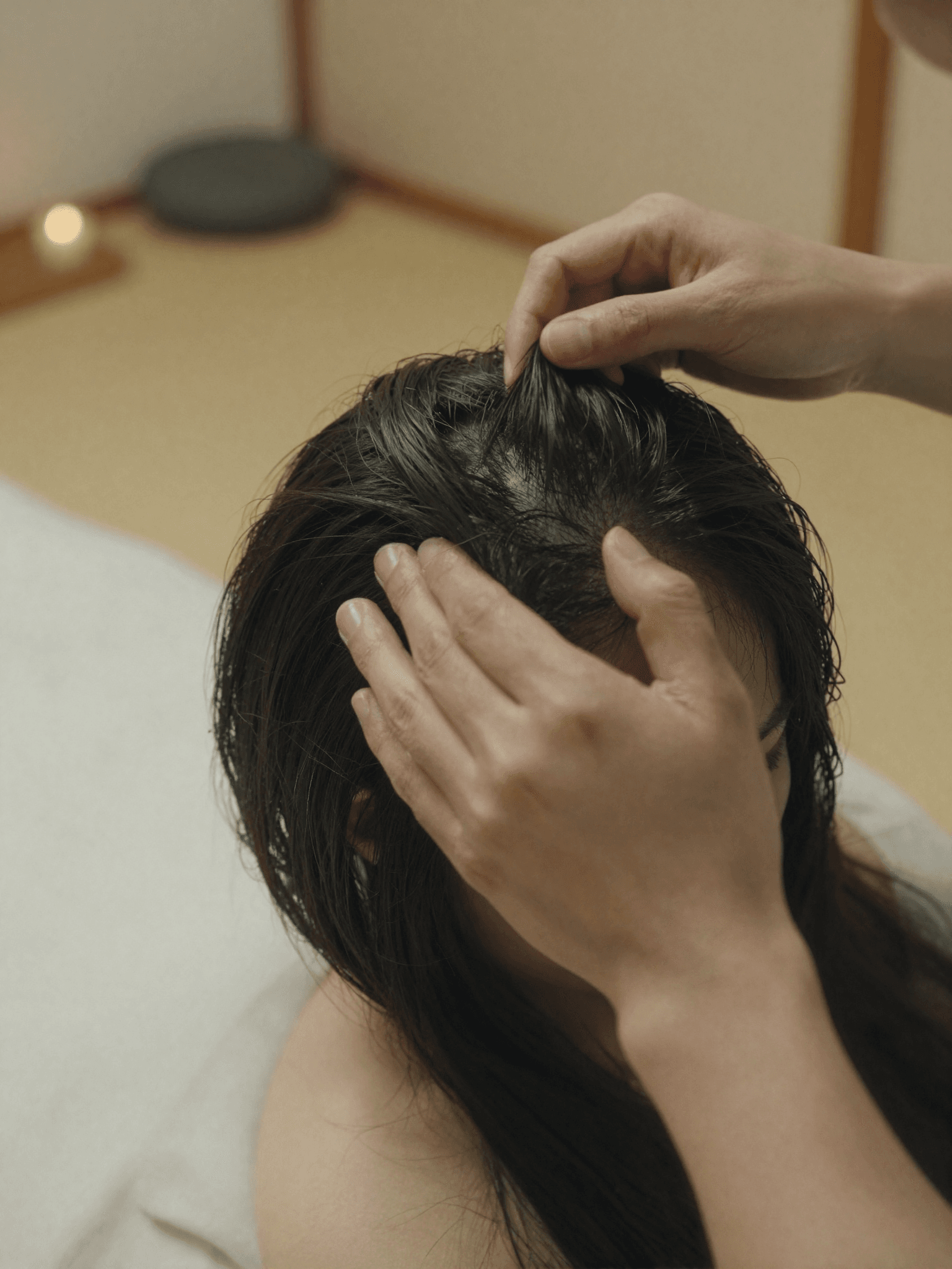 A therapist's hands part a client's hair to closely examine the scalp during a Japanese diagnostic ritual