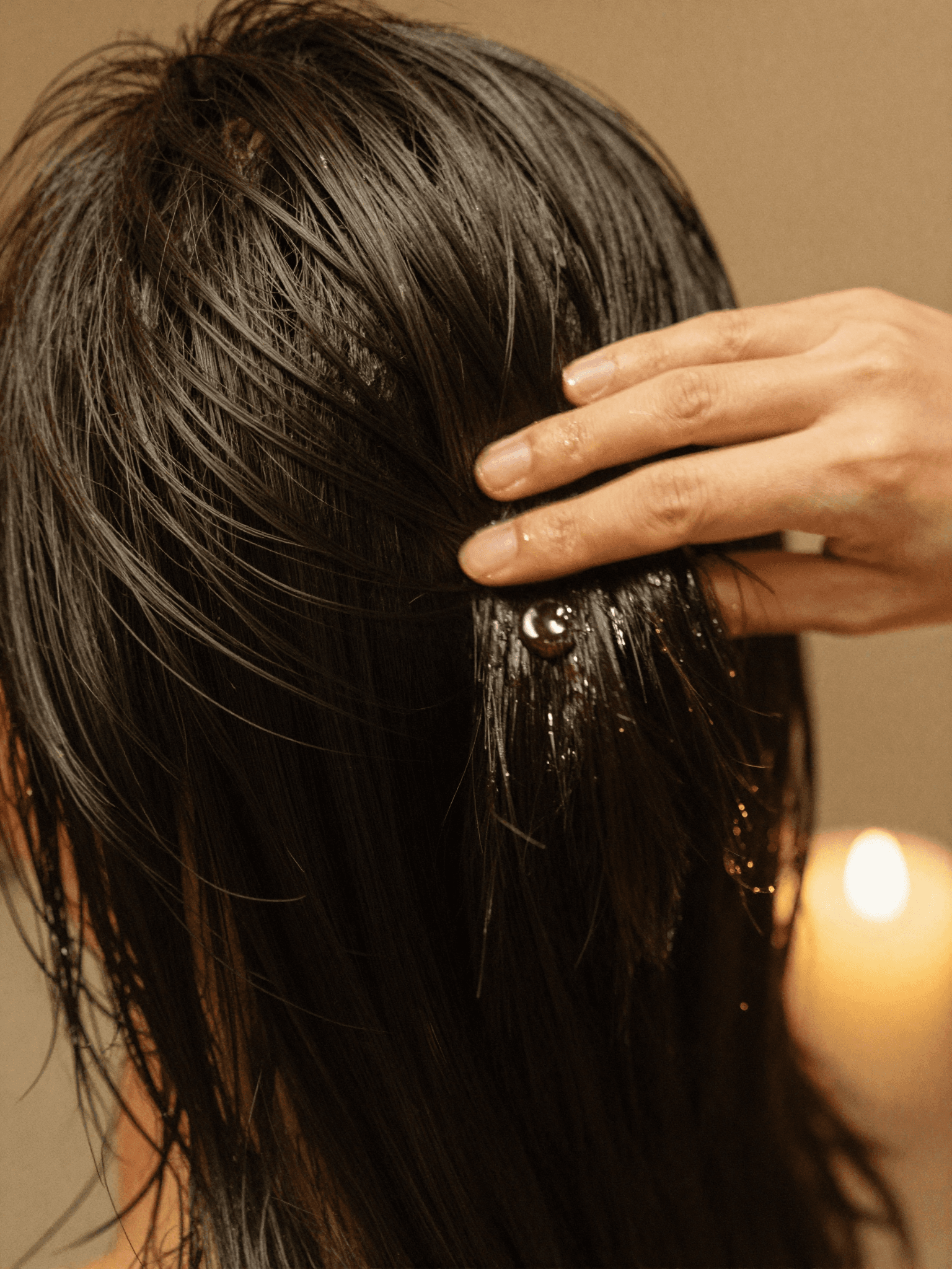 A therapist's hand smooths glistening camellia oil through glossy, healthy hair during the closing ritual