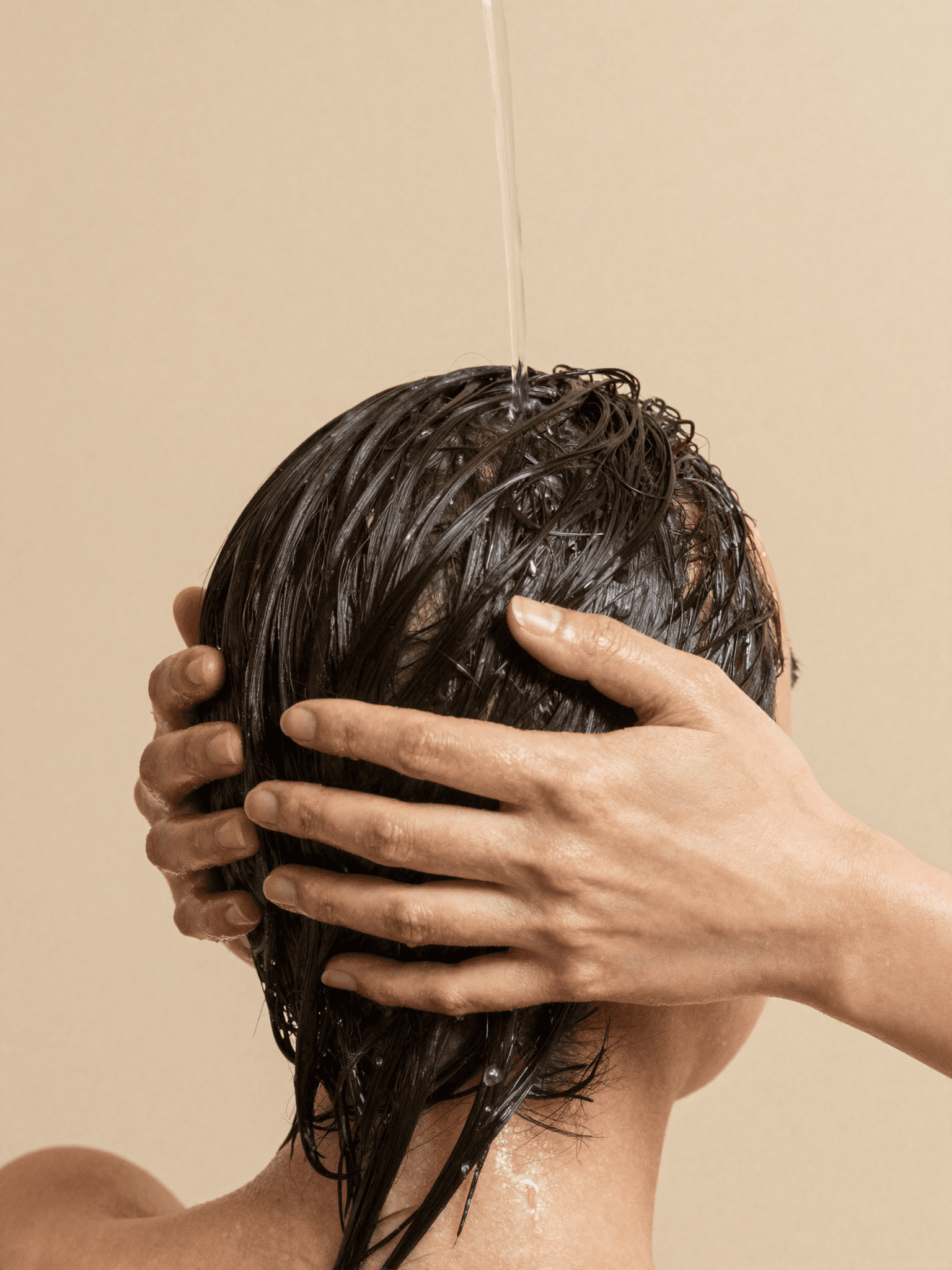 Warm water flowing through dark hair during a deep cleansing ritual, hands working through wet strands